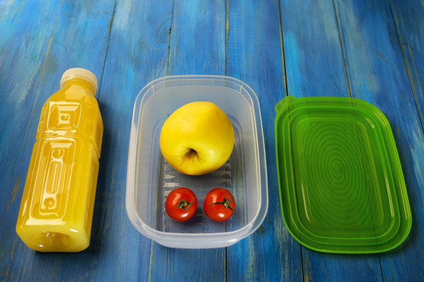 Πλαστικό κουτί φαγητού με μεγάλο ώριμο μήλο και δύο ντοματίνια  - Φωτογραφία, εικόνα