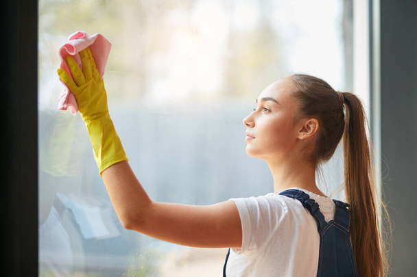 concepto de limpieza. muchacha joven en guantes limpieza ventana grande
 - Foto, Imagen
