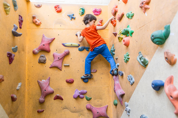 Boy climbing on artificial boulders wall in gym - Фото, изображение
