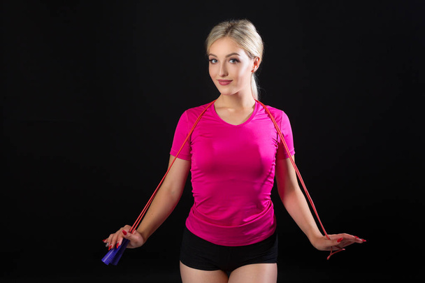 beautiful young woman in sportswear with a skipping rope on a black background - Fotó, kép