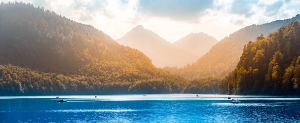 Panoramic view of lake Alpsee with tourists boating and relaxing. Tourism in Hohenschwangau village and Neuschwanstein castle - 写真・画像