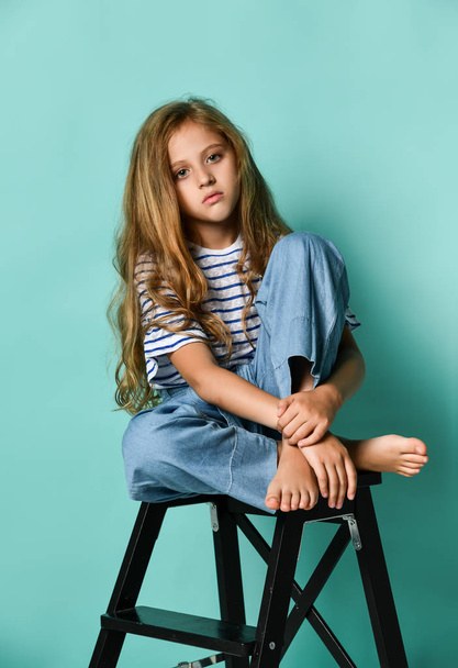Stylish little girl child wearing summer or autumn jeans clothes sitting on a high chair in the studio. - Φωτογραφία, εικόνα