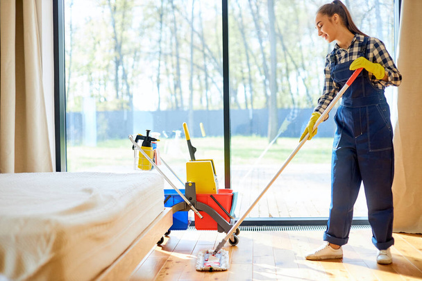 Beautiful young woman cleaner cleaning floor at home using mop - 写真・画像