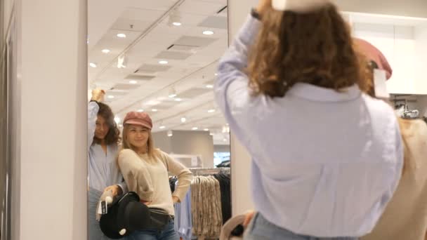 Vtipné nejlepší přítelkyně vyzkoušet klobouky v obchodě s oblečením před zrcadlem a smát - Záběry, video