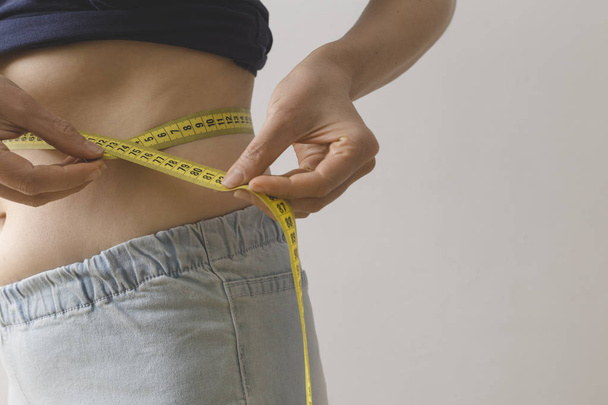 Uma jovem mulher mede a cintura com uma fita métrica. O conceito de perda de peso. - Foto, Imagem