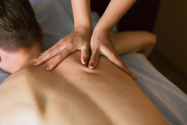 Kobieta masaże pod łopatką na plecach. Masażysta robi masaż dla mężczyzny leżącego na kanapie - Zdjęcie, obraz