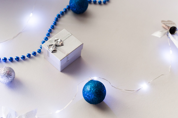 青のガーランドとクリスマスツリーボールとベージュの背景に弓とシルバーの小さな贈り物。新年とクリスマスの概念。トップビュー、フラットレイアウト - 写真・画像