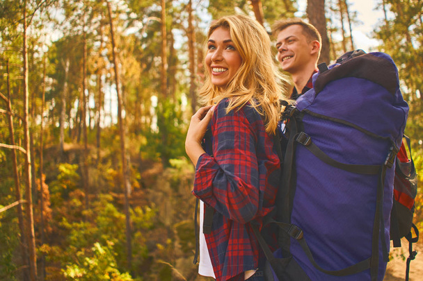 若い男とバックパックを持つ女性は、森林歩道に沿って山の中でハイキングに行きます。森の中を二人の観光客と.  - 写真・画像