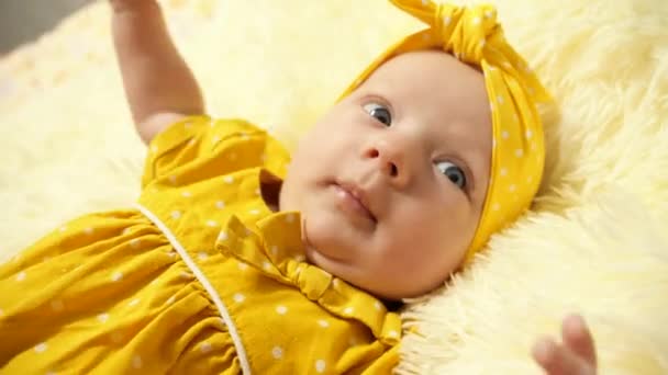Portrait. Bébé dans une robe jaune et un pansement jaune sur la tête, s'amusant à sourire et à gesticuler
. - Séquence, vidéo