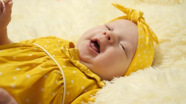Dziecko w żółtej sukience w kropki i żółtym bandażu na głowie uśmiecha się i pokazuje język.. - Materiał filmowy, wideo