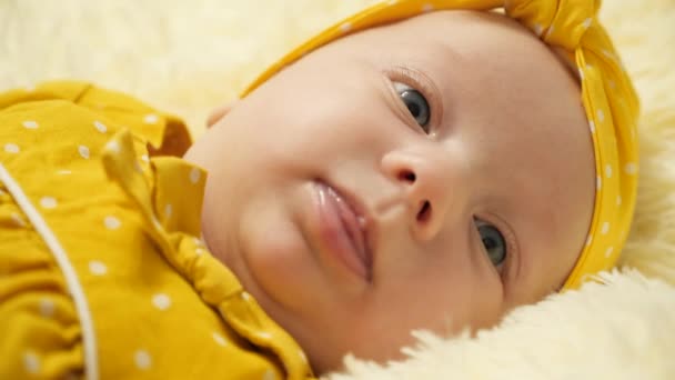 Egy sárga pöttyös ruhás kisbaba, sárga kötéssel a fején mosolyog és megmutatja a nyelvét. Közelkép - Felvétel, videó
