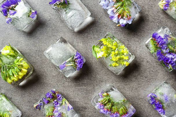 Ice cubes with flowers on grey stone background, flat lay - Photo, image