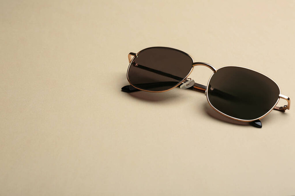 Κομψά γυαλιά ηλίου σε μπεζ φόντο, χώρος για κείμενο. Μοντέρνο αξεσουάρ - Φωτογραφία, εικόνα