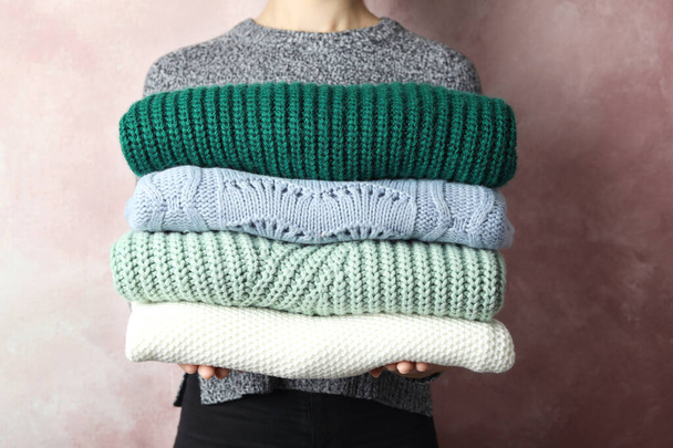Woman holding stack of warm clothes on light background, closeup. Autumn season - 写真・画像