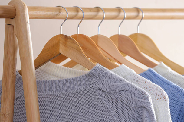 Collection of warm sweaters hanging on rack near light wall, closeup - Fotografie, Obrázek