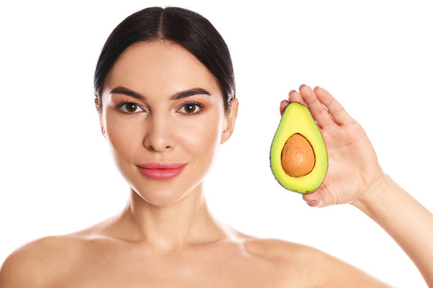 Young woman with silky skin after face mask holding avocado on white background - Фото, зображення