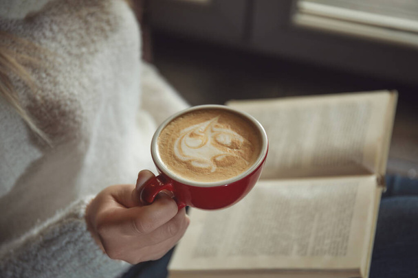 Woman with cup of coffee reading book near window indoors, closeup - Foto, immagini