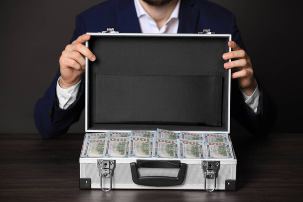 Businessman with case of dollar bills at wooden table, closeup - Фото, изображение