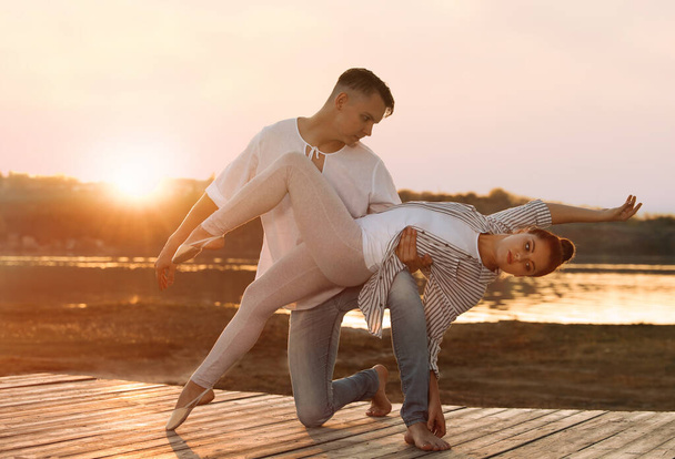 Beautiful young couple practicing dance moves near river at sunset - Фото, зображення