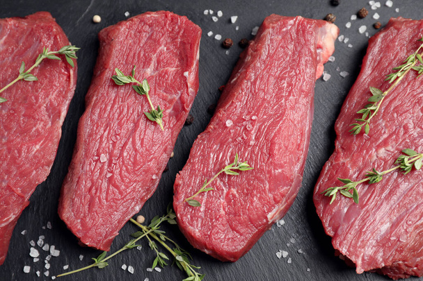 Flat lay composition with fresh meat steaks on black table - Φωτογραφία, εικόνα