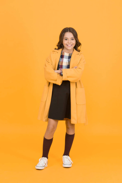 Get cozy in style this autumn season. Happy small girl wear comfortable fashion style. Little child with long brunette hair style smile orange background. Bringing some chic vibes to school style - Zdjęcie, obraz