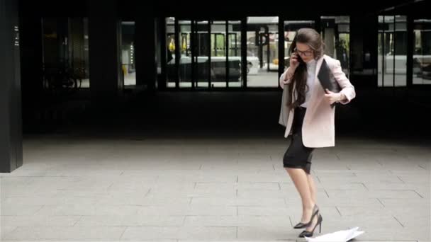 Молода стресовий бізнес жінка в окулярах проходить через місто з документами і розмовами по телефону. Вона кидає свої документи для стресу
. - Кадри, відео