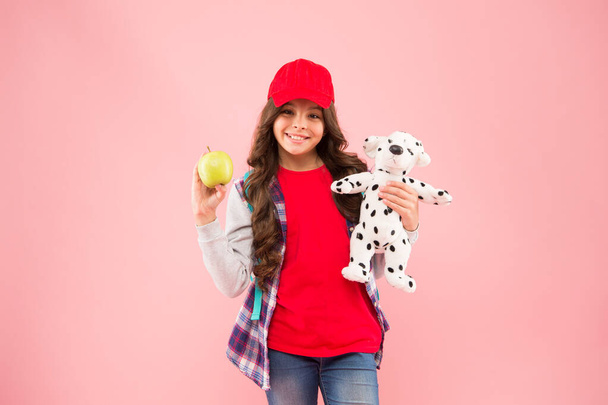 Reduce stress. Healthy lifestyle. Mental and physical wellbeing. Schoolgirl daily life. Stylish schoolgirl. Girl little fashionable schoolgirl with backpack carry soft toy dog and hold apple - Foto, afbeelding