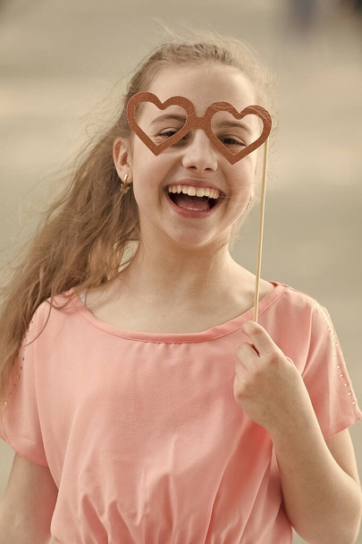 Happy valentines day. Small child with happy smile and funny look through heart shaped glasses. Happy little girl smiling with photobooth props on stick. Celebrating happy international childrens day - Zdjęcie, obraz
