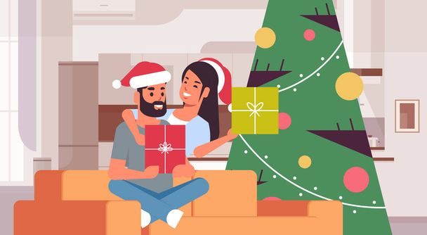 couple holding gift boxes merry christmas happy new year holiday celebration concept man woman embracing wearing santa hats sitting on couch near fit tree modern living room interior horizontal - Вектор, зображення