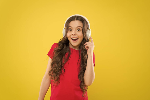Technology is wonderful when it works. Happy little girl listening to music in earphones on yellow background. Small child enjoying stereo sound technology. New technology. Technology concept - Foto, Bild