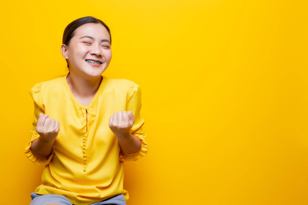 Šťastná žena, aby vítězné gesto izolované přes žluté pozadí - Fotografie, Obrázek
