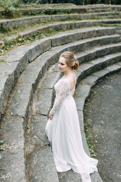 Wedding in the European style in nature. A bride in a white dress on a stone staircase.  - Photo, image