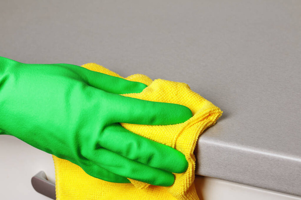 Крупный план руки в защитной перчатке, держащей салфетку и вытирающей столешницу. Уборка кухни
 - Фото, изображение