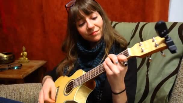Dziewczyna gra ukulele w salonie.  - Materiał filmowy, wideo