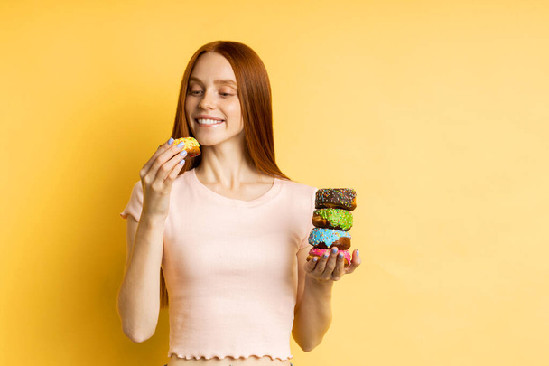 Young beautiful woman with doughnuts on yellow background - Фото, зображення