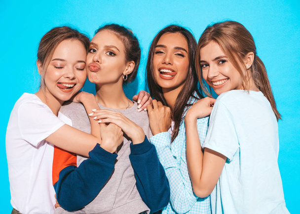 Négy fiatal, gyönyörű, mosolygós hipster lány divatos nyári ruhában. Szexi, gondtalan nők pózolnak a kék fal mellett a stúdióban. Pozitív modellek szórakozás és ölelés - Fotó, kép