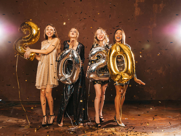 Hermosas mujeres celebrando el Año Nuevo. Chicas hermosas felices en vestidos de fiesta sexy con estilo celebración de oro y plata 2020 globos, divirtiéndose en la fiesta de fin de año. Celebración de vacaciones. Modelos con encanto
  - Foto, Imagen