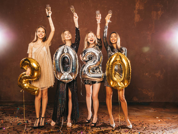 schöne Frauen, die Neujahr feiern.happy wunderschöne Mädchen in stilvollen sexy Partykleidern mit goldenen und silbernen Luftballons 2020, Spaß an der Silvesterparty haben.arrying und Champagnerflöten trinken - Foto, Bild
