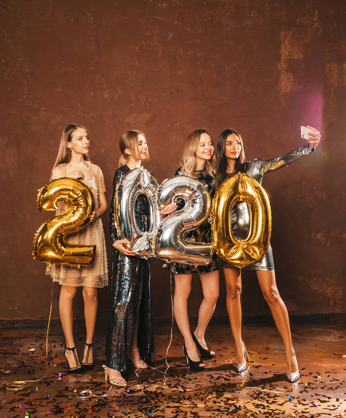 Hermosas mujeres celebrando año nuevo. Chicas hermosas felices en vestidos de fiesta sexy con estilo celebración de oro y plata 2020 globos, divirtiéndose en la víspera de Año Nuevo Party.arrying y beber flautas de champán
 - Foto, imagen