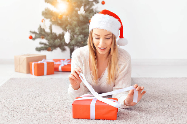 Mujer rubia bonita con un suéter de punto cálido, acostada en una alfombra cerca del árbol de Navidad decorado en una sala de estar. Un montón de regalos bajo el árbol
. - Foto, Imagen
