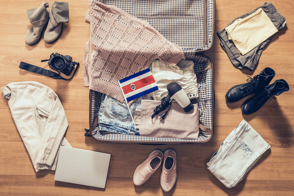 Vêtements de femme, ordinateur portable, appareil photo et drapeau du Costa Rica couché sur le parquet près et dans la valise ouverte. Concept de voyage
 - Photo, image