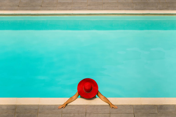 Gyönyörű lány fürdőruhában és piros sapkában egy kék medencében. - Fotó, kép