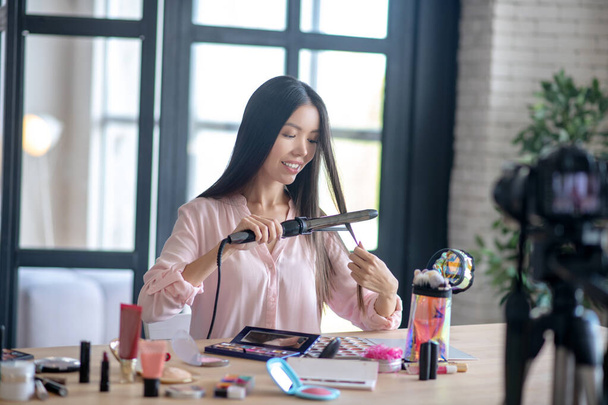 Long-haired woman curling her hair in the morning while filming blog - Fotó, kép