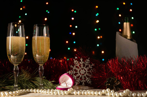 Dîner romantique de Noël et du Nouvel An d'un couple amoureux de deux verres de champagne et d'une alliance. Branche d'épinette et de mousseline rouge sur une table sur un fond sombre avec des lumières floues
. - Photo, image