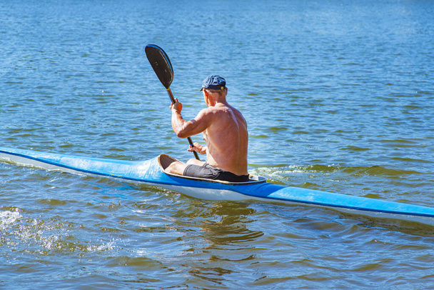 男は海岸近くの川に青と黄色のカヤックを漕いでいる。カヤックのコンセプト男が川のカヌーで泳ぐ。晴れた夏の日にボートに乗った男。青と黄色のボート. - 写真・画像