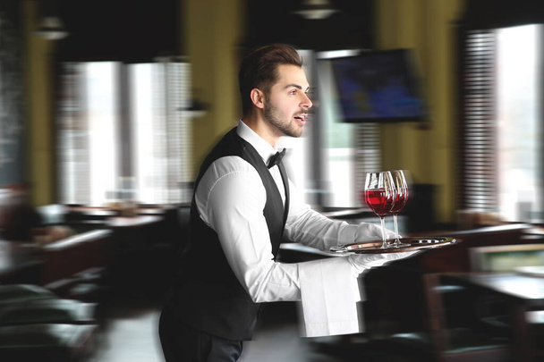 Young hurrying waiter with glasses of wine in restaurant - 写真・画像