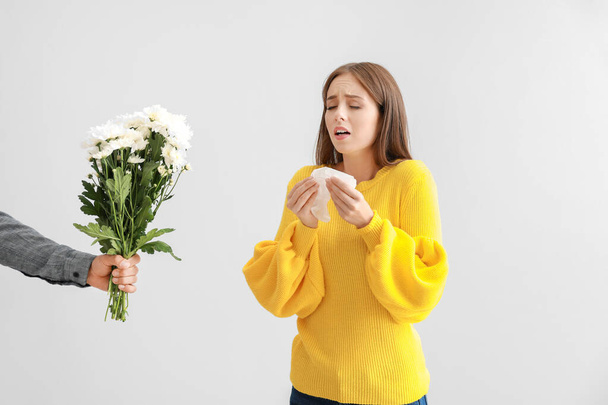 Man giving flowers to young woman suffering from allergy on light background - Фото, изображение