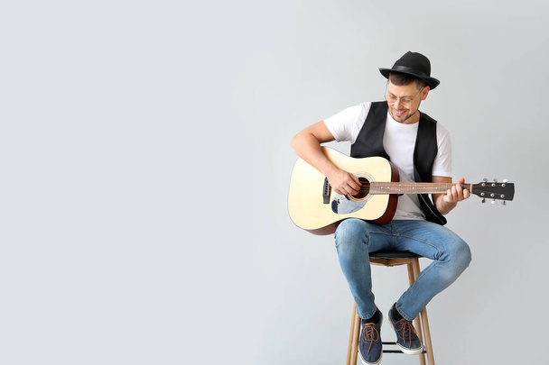 Όμορφος άντρας παίζει κιθάρα σε ελαφρύ φόντο - Φωτογραφία, εικόνα