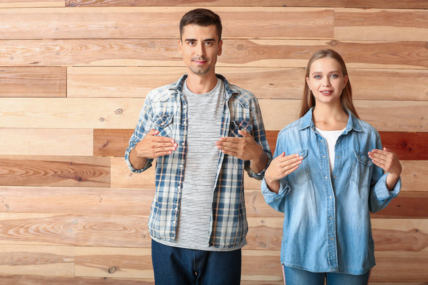 Giovane coppia sordomuta utilizzando il linguaggio dei segni su sfondo di legno
 - Foto, immagini