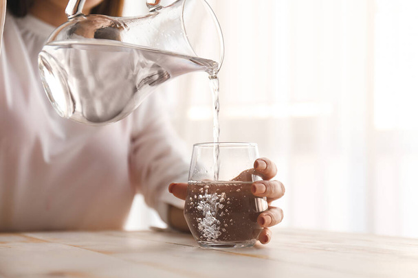 Nő öntés friss vizet kancsó üvegbe az asztalon - Fotó, kép